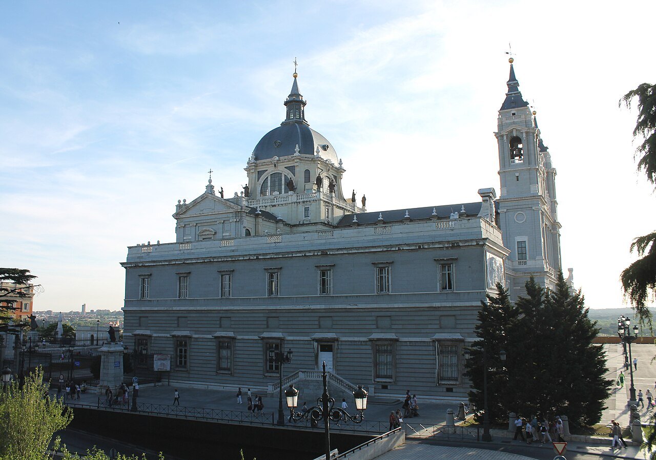 The pale stone east façade of Almudena Cathedral in Madrid with its dome and two towers, behind trees