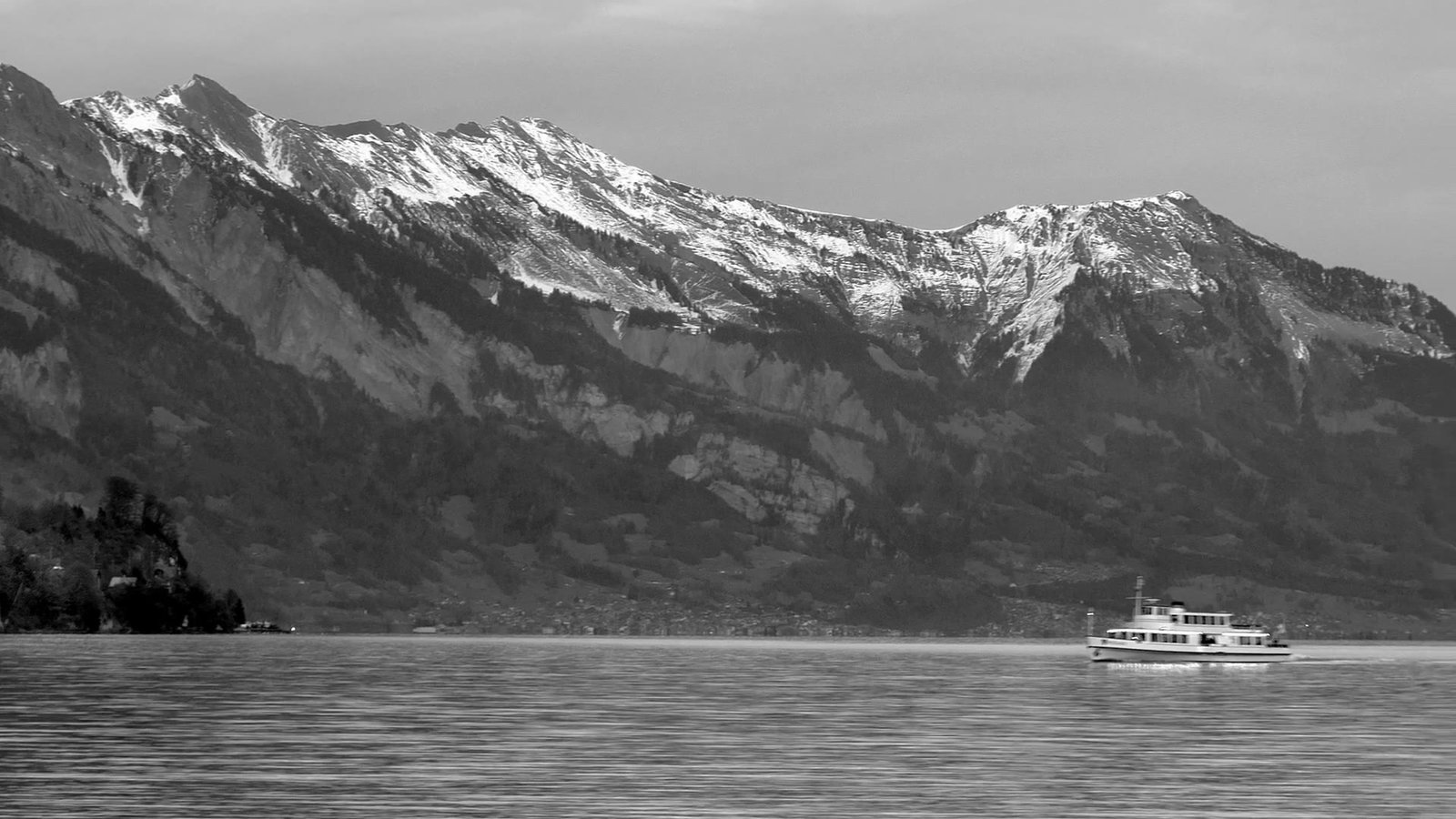 Black and white photo of snowy mountains above a lake near Interlaken with a boat