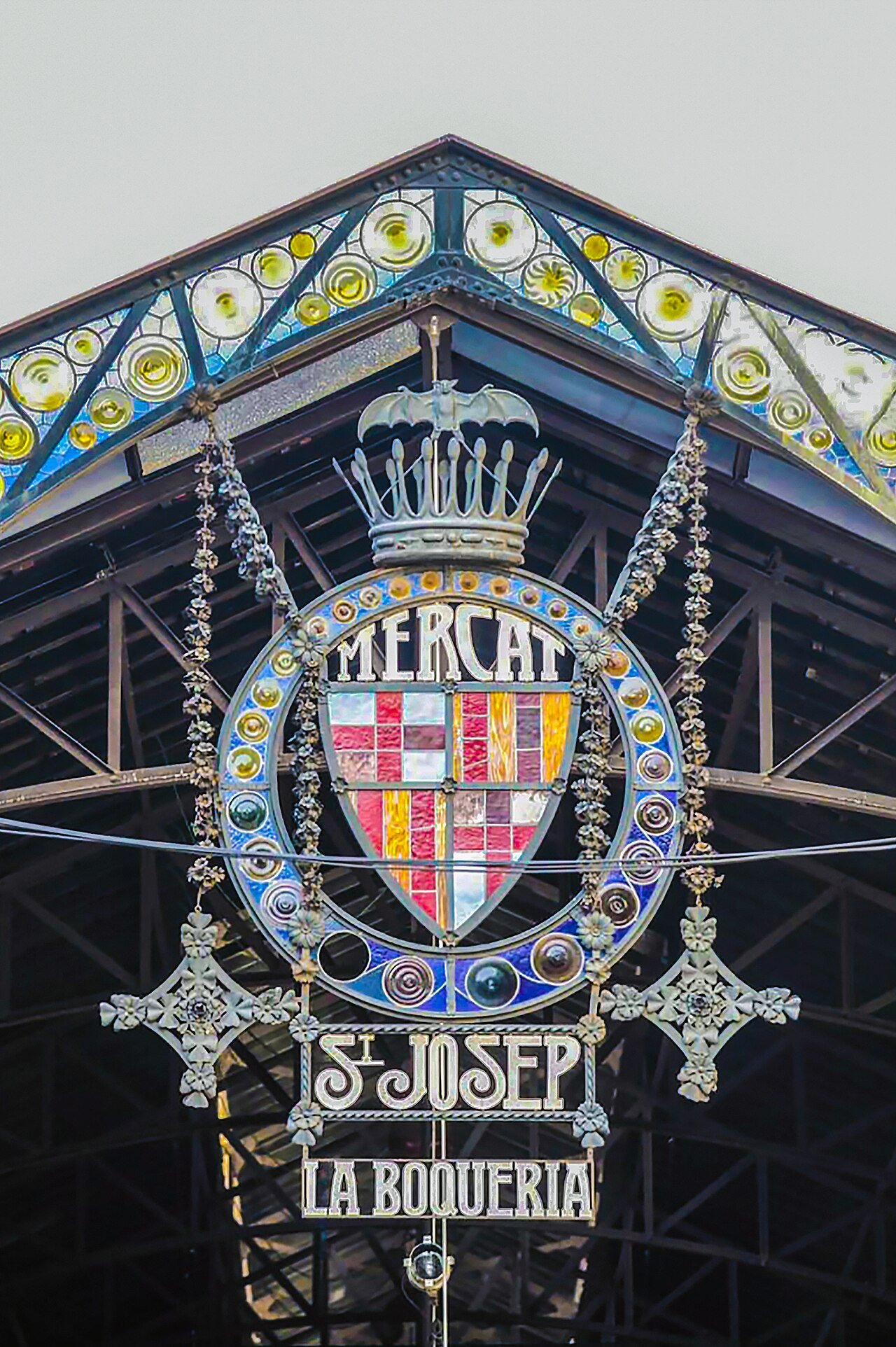 The decorated iron and stained-glass entrance arch of La Boqueria market in Barcelona, with the city coat of arms and the words Mercat St Josep La Boqueria