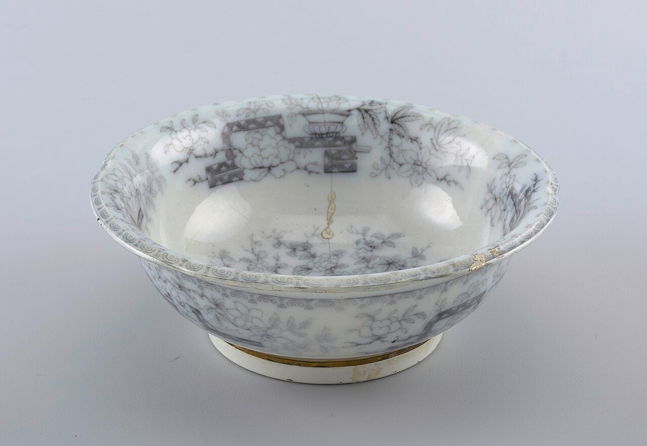 A white 19th-century bowl with grey Chinese-style flowers; a crack running down the inside has been repaired with a thin line of gold