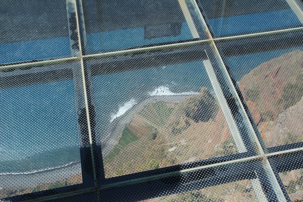 Looking down through the glass floor of the Cabo Girão skywalk in Madeira to the cultivated fields at the foot of the cliff