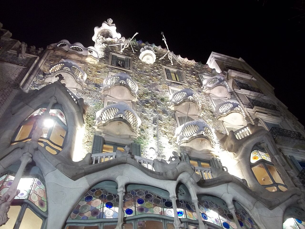 The upper façade of Casa Batlló in Barcelona lit up at night, with its bone-like balconies, coloured glass and scaly roof
