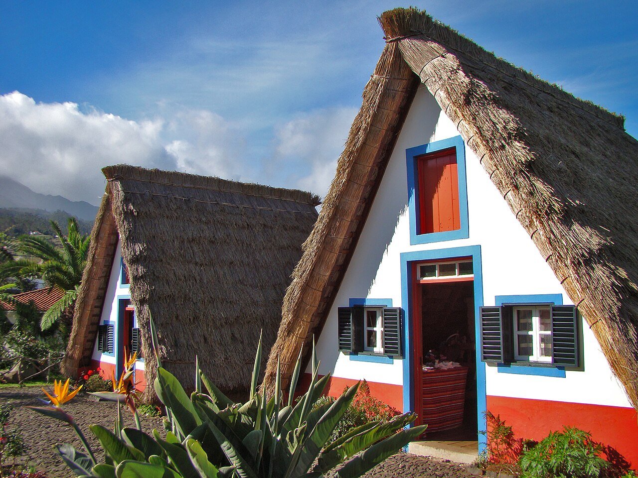 Two traditional triangular Casas de Santana in Madeira, white with red doors, blue trim and steep thatched roofs