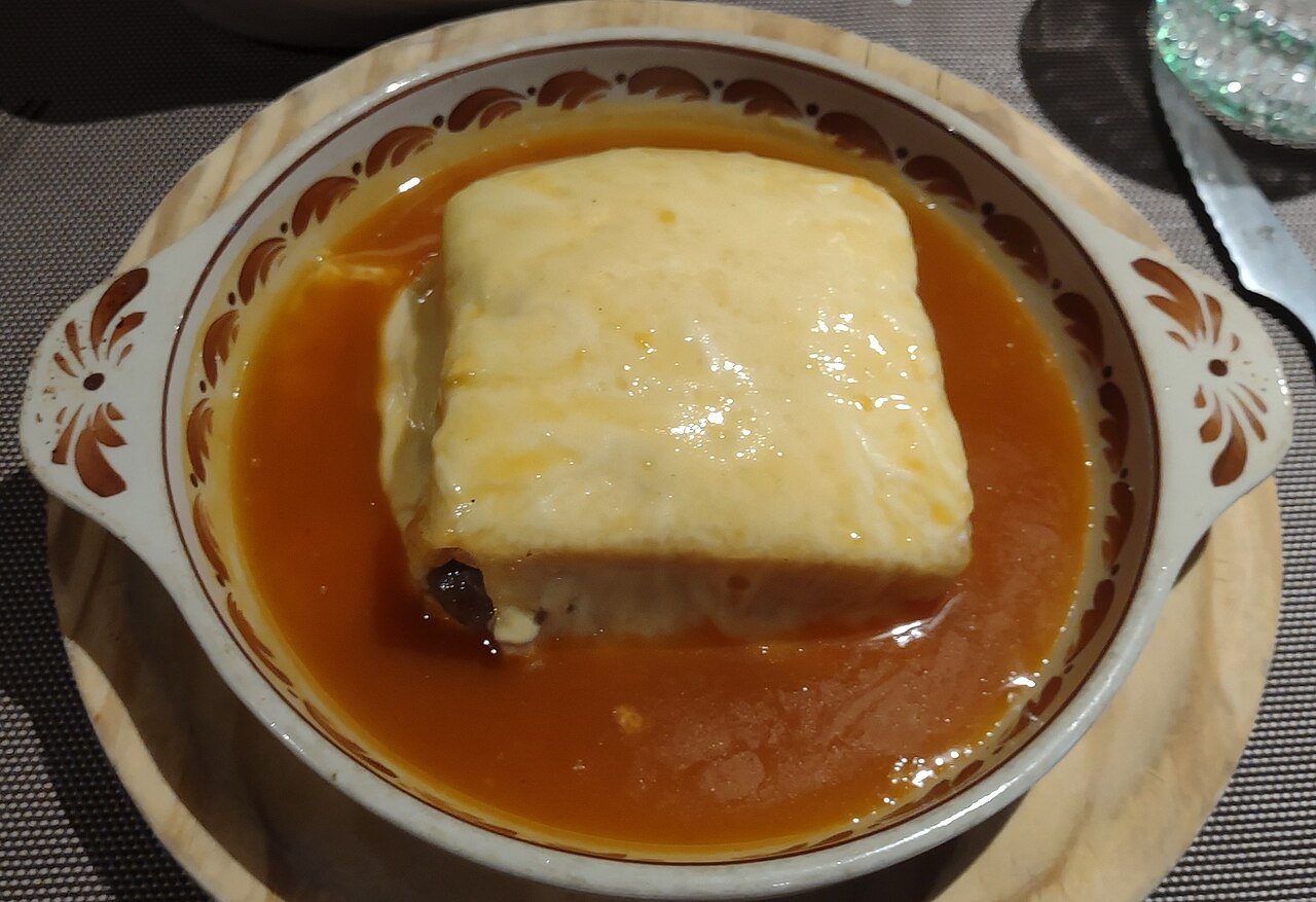 A francesinha in Porto: a layered sandwich covered in melted cheese, sitting in a dish of orange tomato-and-beer sauce
