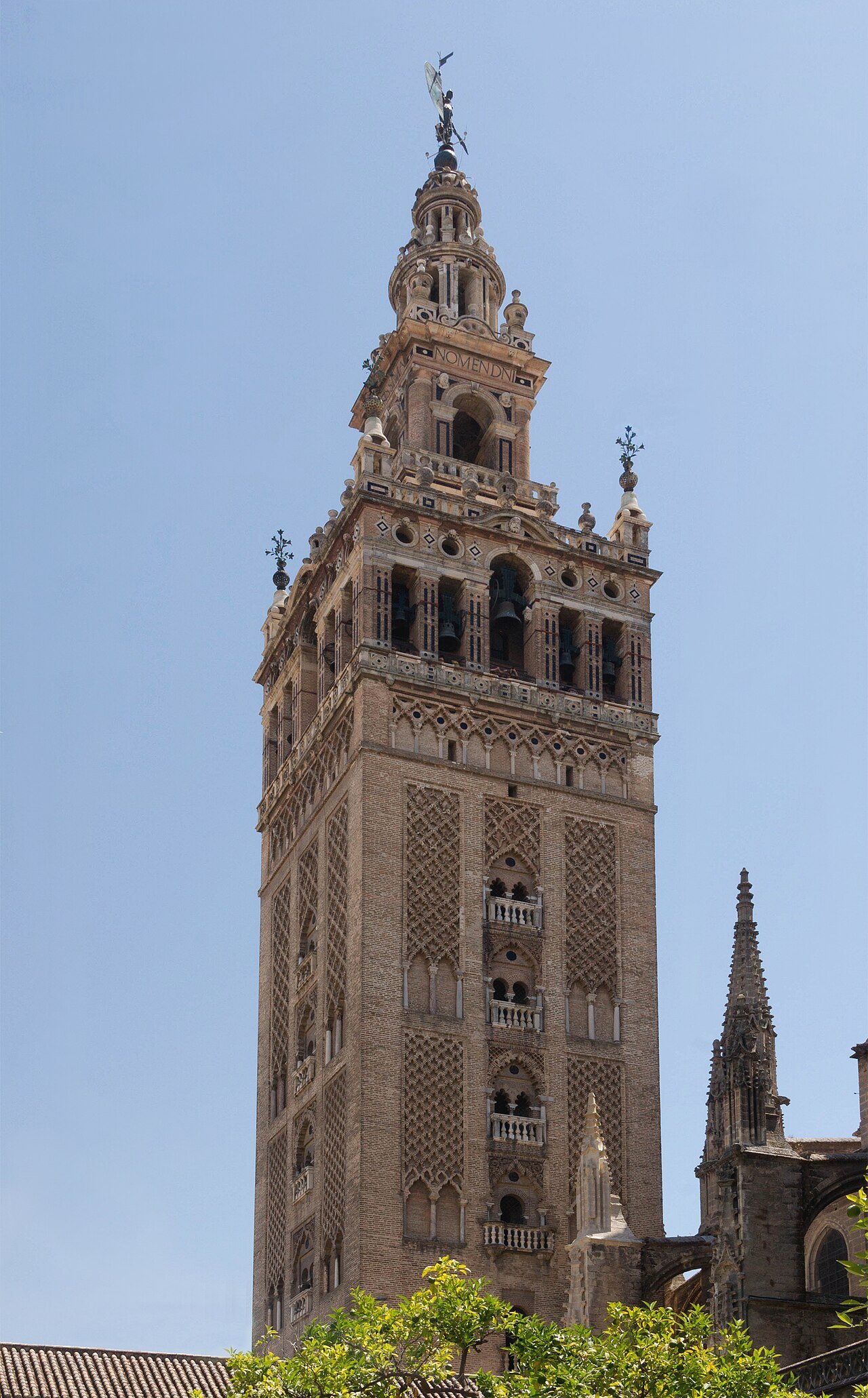 The Giralda bell tower of Seville Cathedral rising above the orange trees of the Patio de los Naranjos under a clear sky