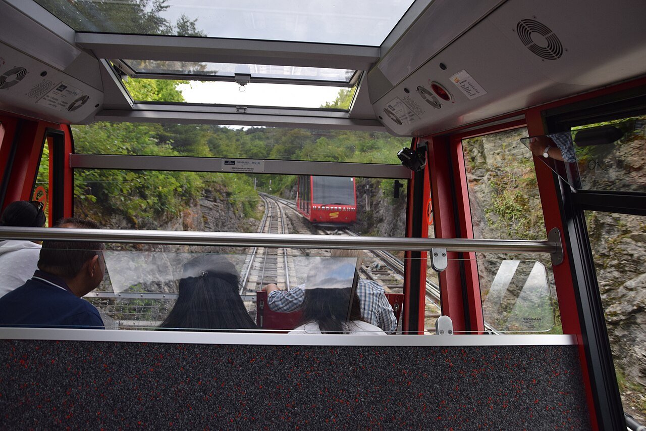 Inside a red Harderbahn funicular car, looking down the steep track through the forest above Interlaken