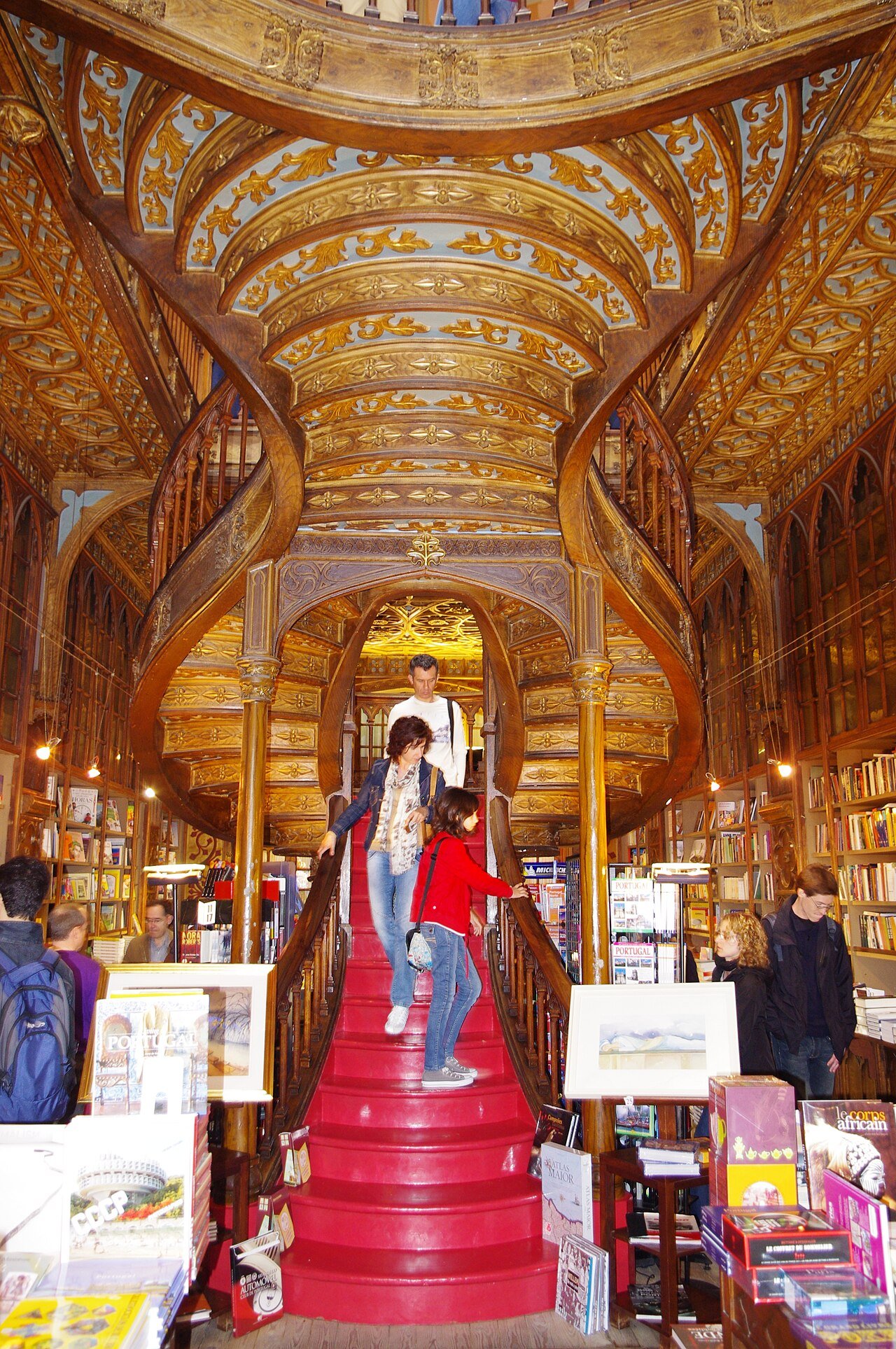 The red central staircase of Livraria Lello in Porto, with carved wooden balustrades, bookshelves and visitors on the steps