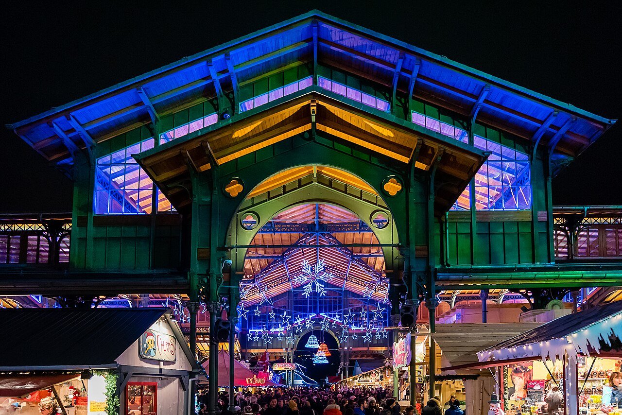 The covered market hall in Montreux lit up in blue, green and gold for the Christmas market, with crowds and stalls below