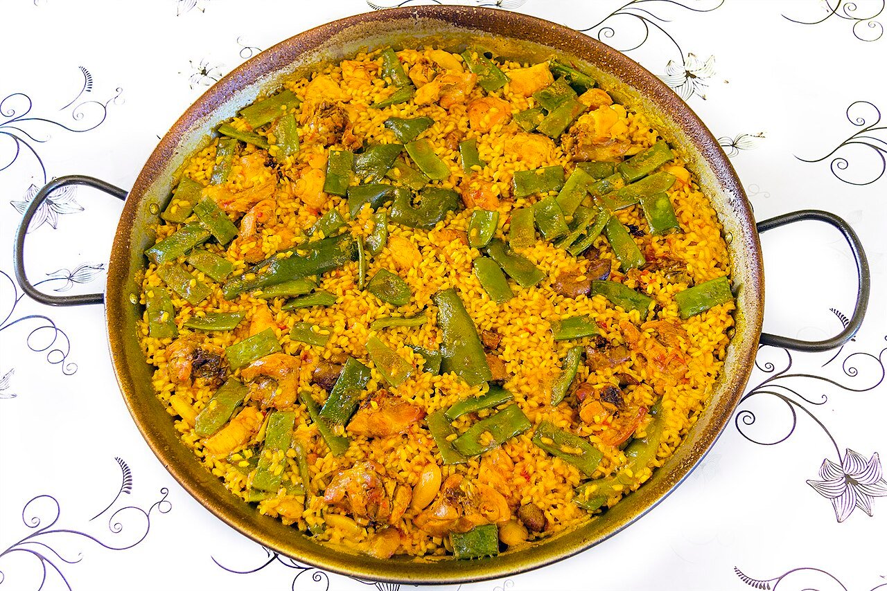 A pan of paella valenciana with rice, green beans and meat, seen from above