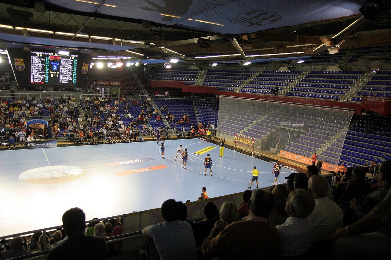 A handball match under way inside the Palau Blaugrana arena in Barcelona, with spectators in the stands