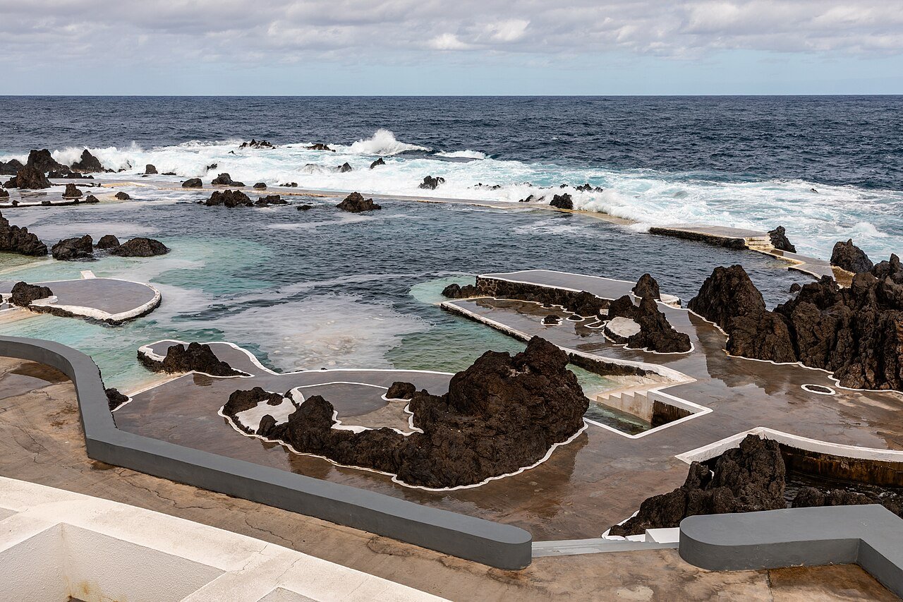 The natural lava pools of Porto Moniz in Madeira: calm seawater pools enclosed by black volcanic rock, with Atlantic waves breaking beyond