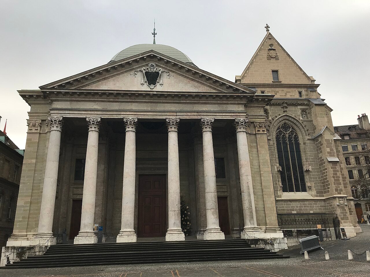 The neoclassical portico of Saint-Pierre Cathedral in Geneva, with columns under a triangular pediment and a Gothic tower beside it