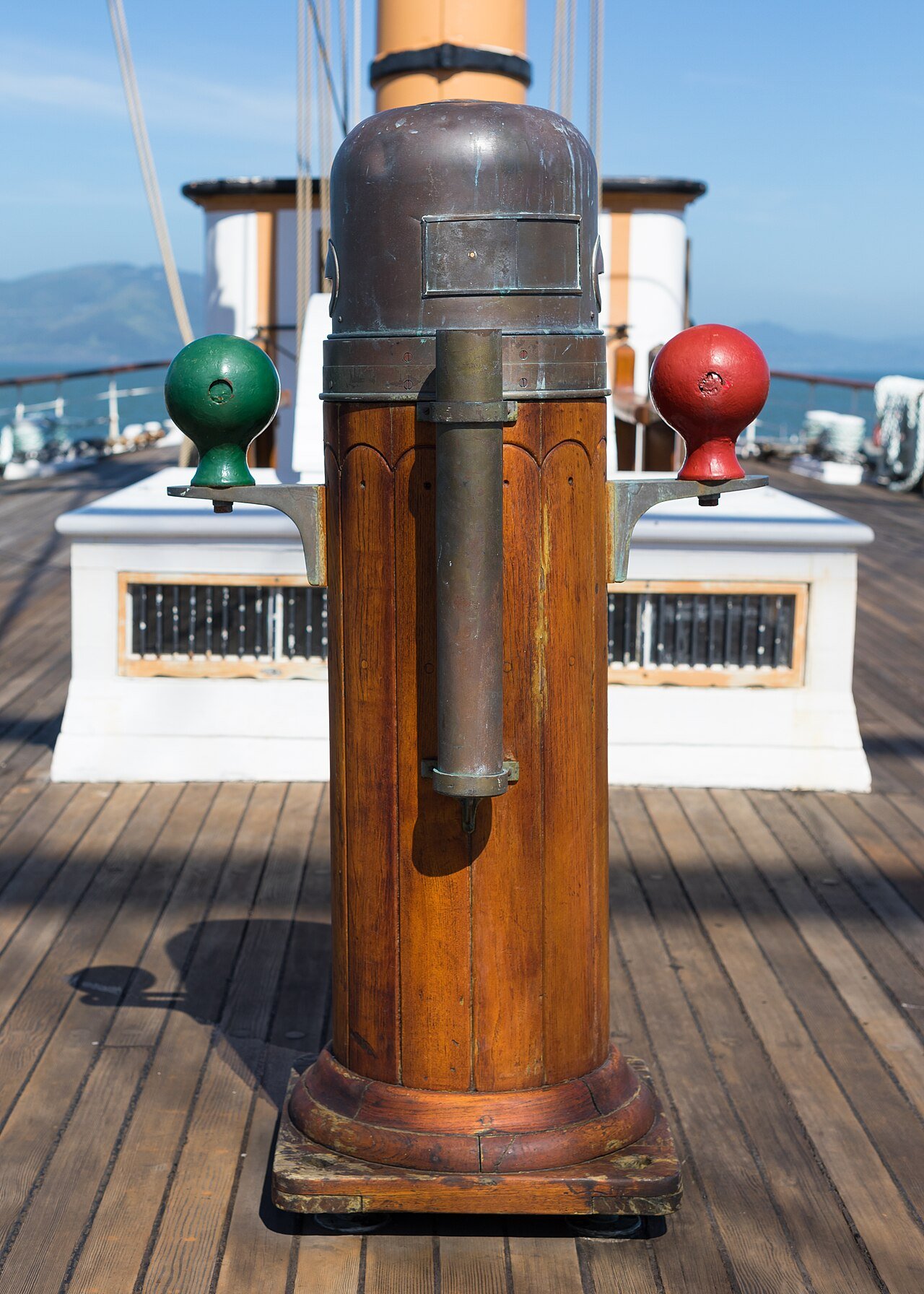 The magnetic compass binnacle on the deck of the sailing ship Balclutha: a brass-domed wooden pillar with a green iron sphere on one side and a red one on the other