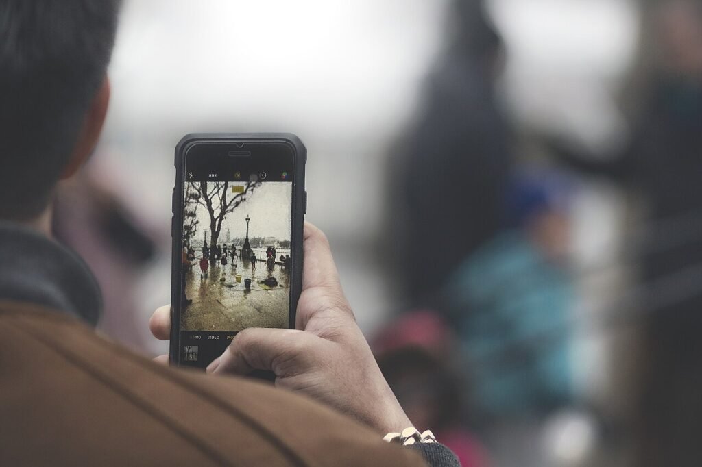 Over-the-shoulder view of a person framing a rainy riverside street scene on a smartphone screen