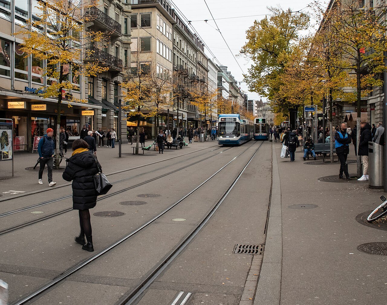 Two blue and white trams on the twin tracks of Bahnhofstrasse in Zurich, with people on the wide pavements