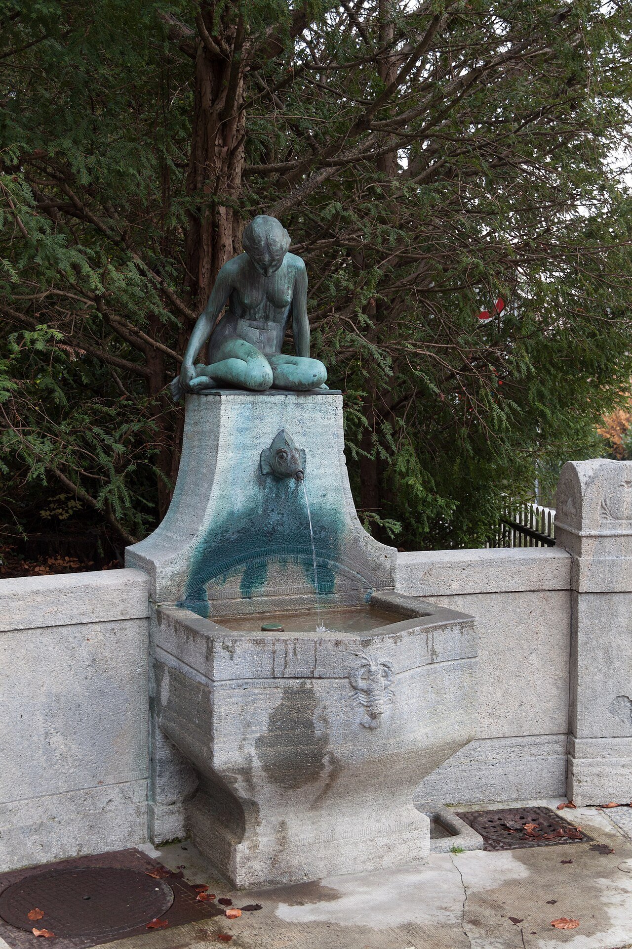 A stone drinking fountain in Zurich topped by a bronze sculpture of a seated figure