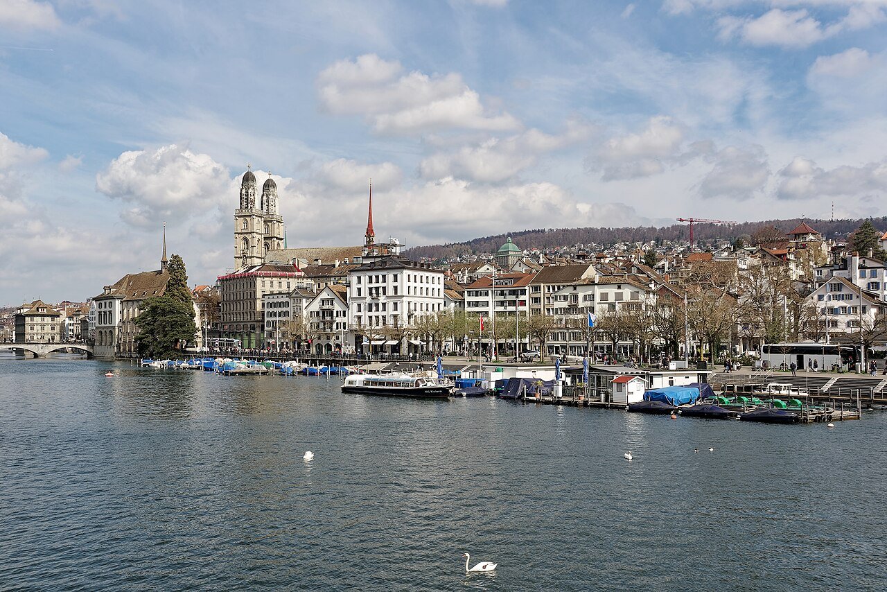 The twin towers of the Grossmünster above the old town houses on the far bank of the River Limmat, with boats and a swan